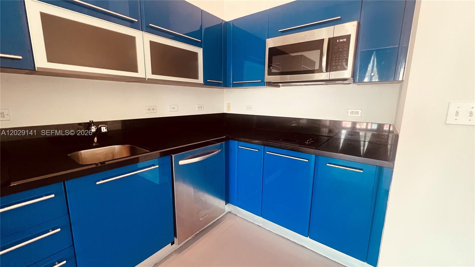 A kitchen features blue glossy cabinets, stainless steel appliances, and black countertops — 253 NE 2nd St # 330, Miami FL 33132, MIAMI, FL