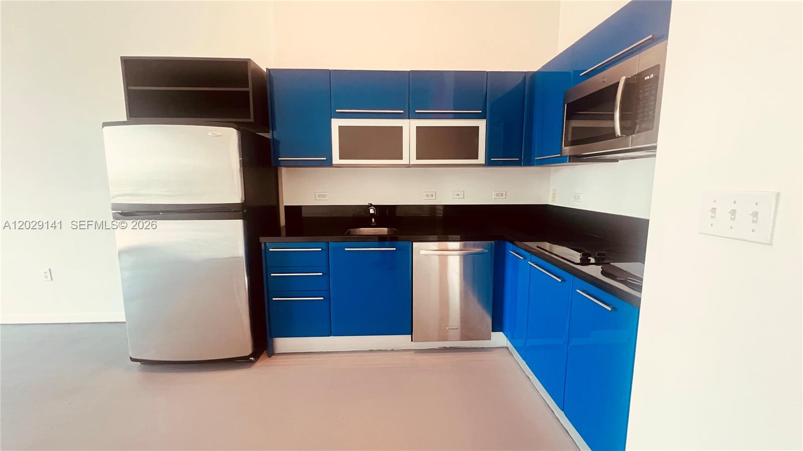 A kitchen with blue cabinets and black countertops leads to a hallway with a door — 253 NE 2nd St # 330, Miami FL 33132, MIAMI, FL