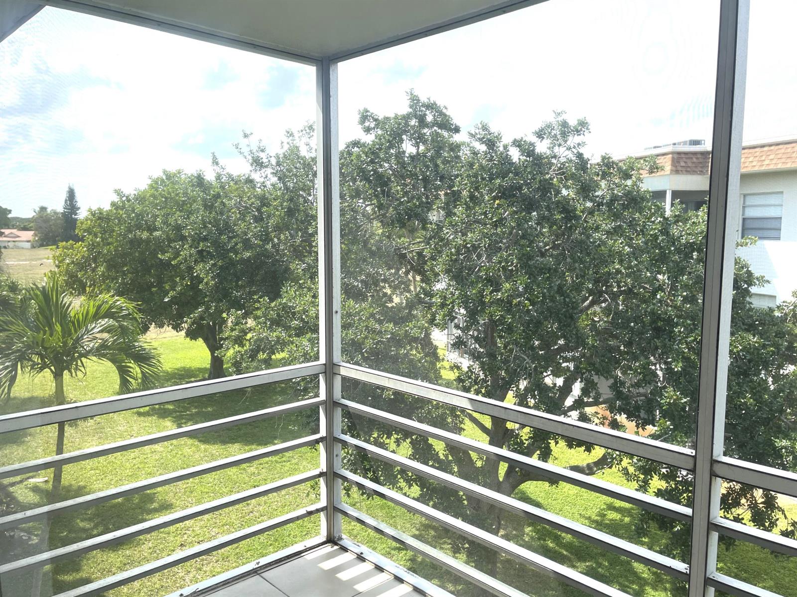 A screened-in balcony overlooks a grassy lawn with mature trees and a neighboring building — 5501 NW 2nd Avenue # 313, Boca Raton FL 33487, BOCA RATON, FL
