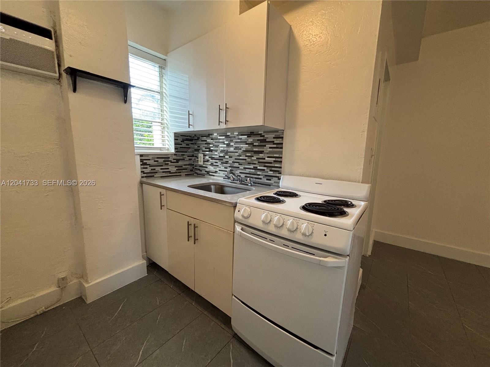 A small kitchen features white cabinets, a stainless steel sink, and a white electric stove — 1843 Dewey St # 110, Hollywood FL 33020, HOLLYWOOD, FL