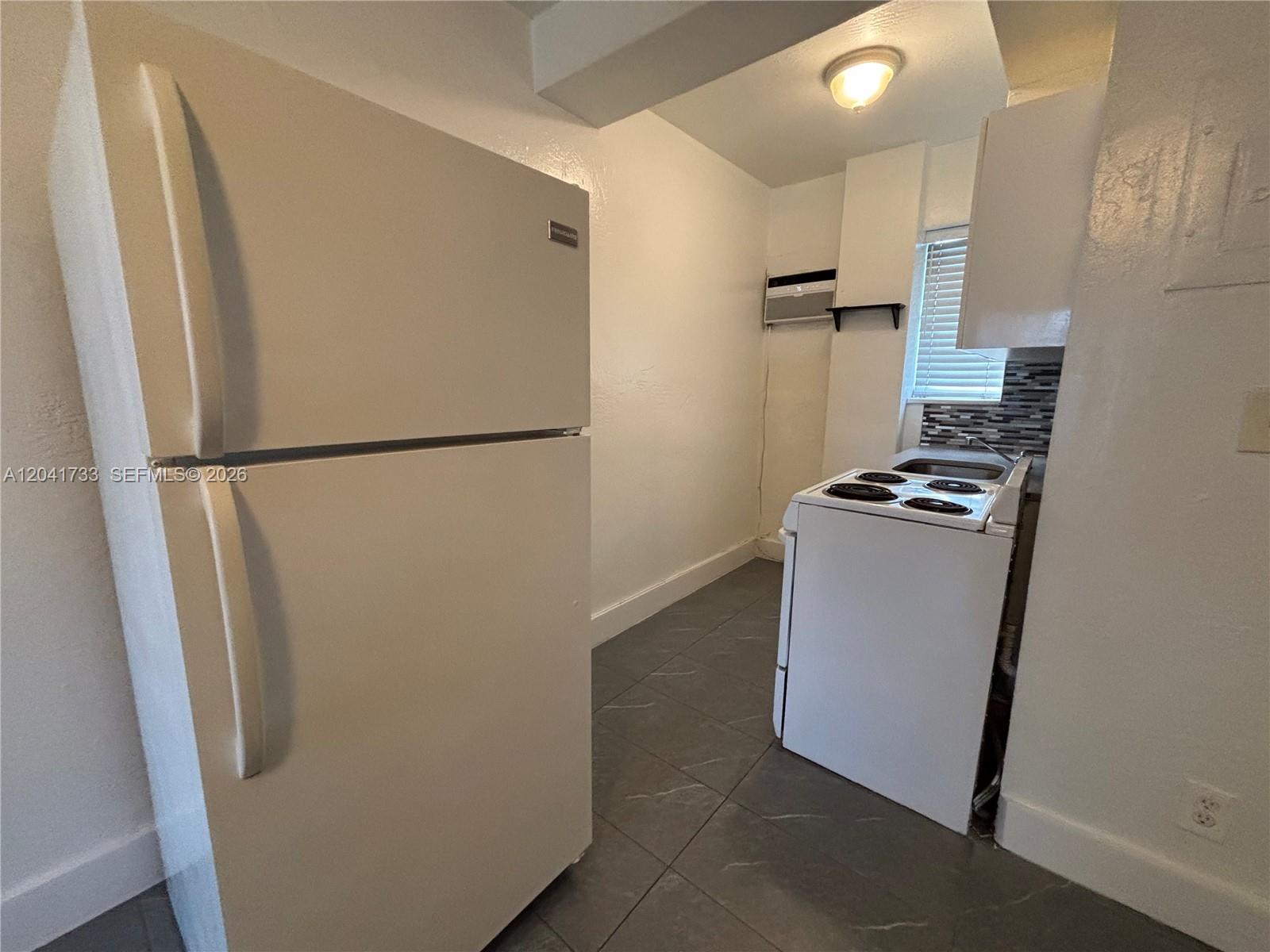 This small kitchen features a white refrigerator, a stove, and gray tiled flooring — 1843 Dewey St # 110, Hollywood FL 33020, HOLLYWOOD, FL