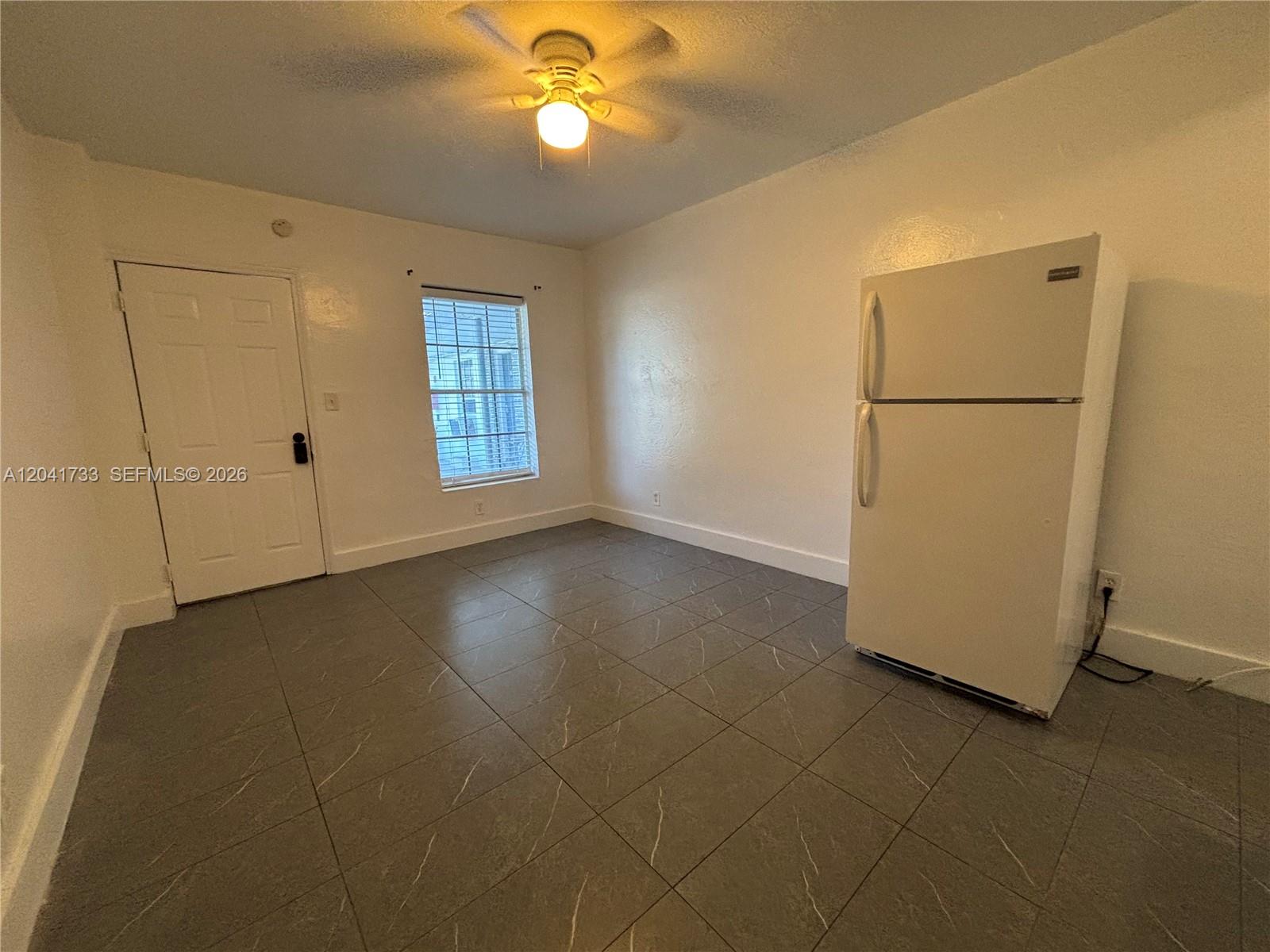 A room with gray tiled floors, a white refrigerator, a window, and a ceiling fan — 1843 Dewey St # 110, Hollywood FL 33020, HOLLYWOOD, FL