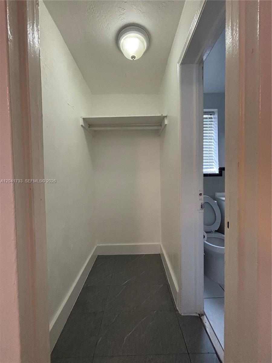 A small closet with a shelf and light fixture leads into a tiled bathroom — 1843 Dewey St # 110, Hollywood FL 33020, HOLLYWOOD, FL