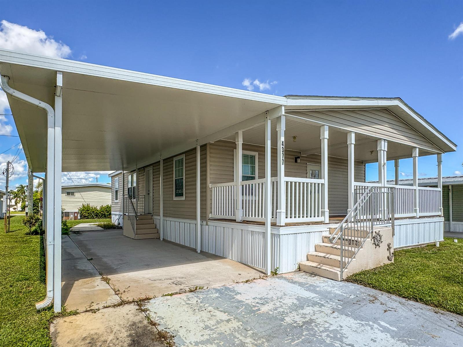 A beige manufactured home features a large carport, a front porch, and concrete steps — 4377 Mission Bell Drive, Boynton Beach FL 33436, BOYNTON BEACH, FL