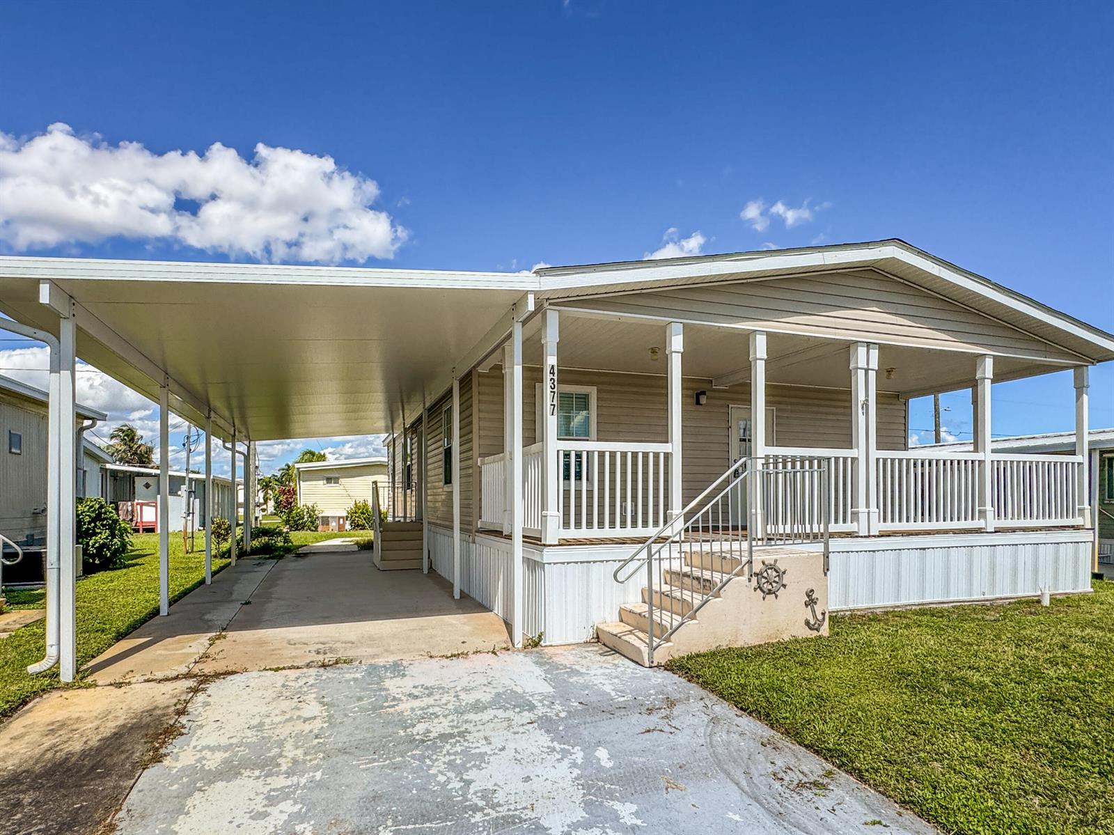 A beige manufactured home features a large carport, a front porch, and a concrete driveway — 4377 Mission Bell Drive, Boynton Beach FL 33436, BOYNTON BEACH, FL