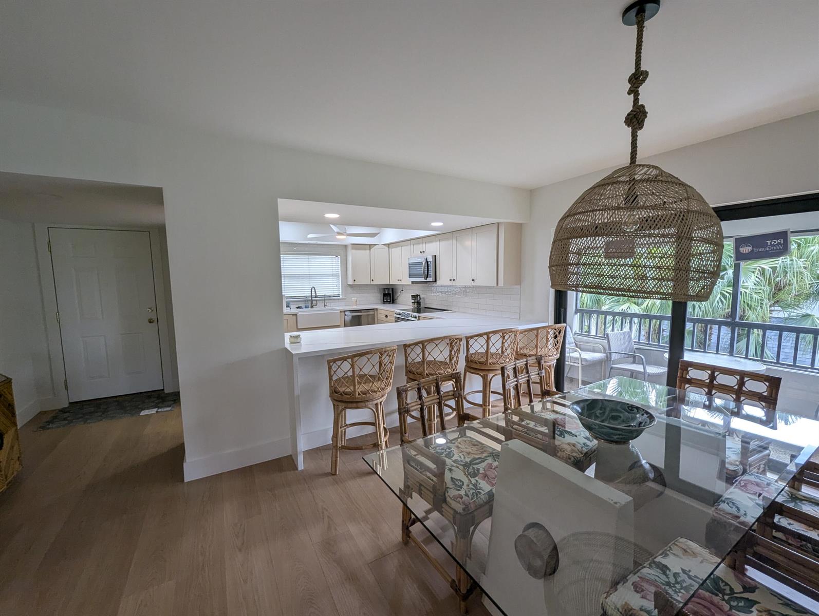 A kitchen with white cabinets and a breakfast bar overlooks a dining area with rattan furniture — 404 Clubhouse Circle, Jupiter FL 33477, JUPITER, FL