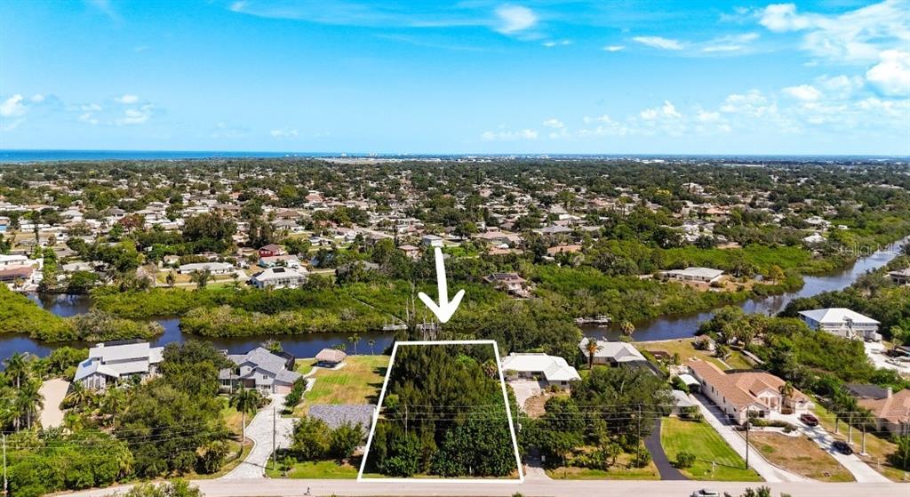An aerial view shows a vacant, tree-covered residential lot outlined in white near a waterway — LEMON BAY DRIVE, VENICE, FL