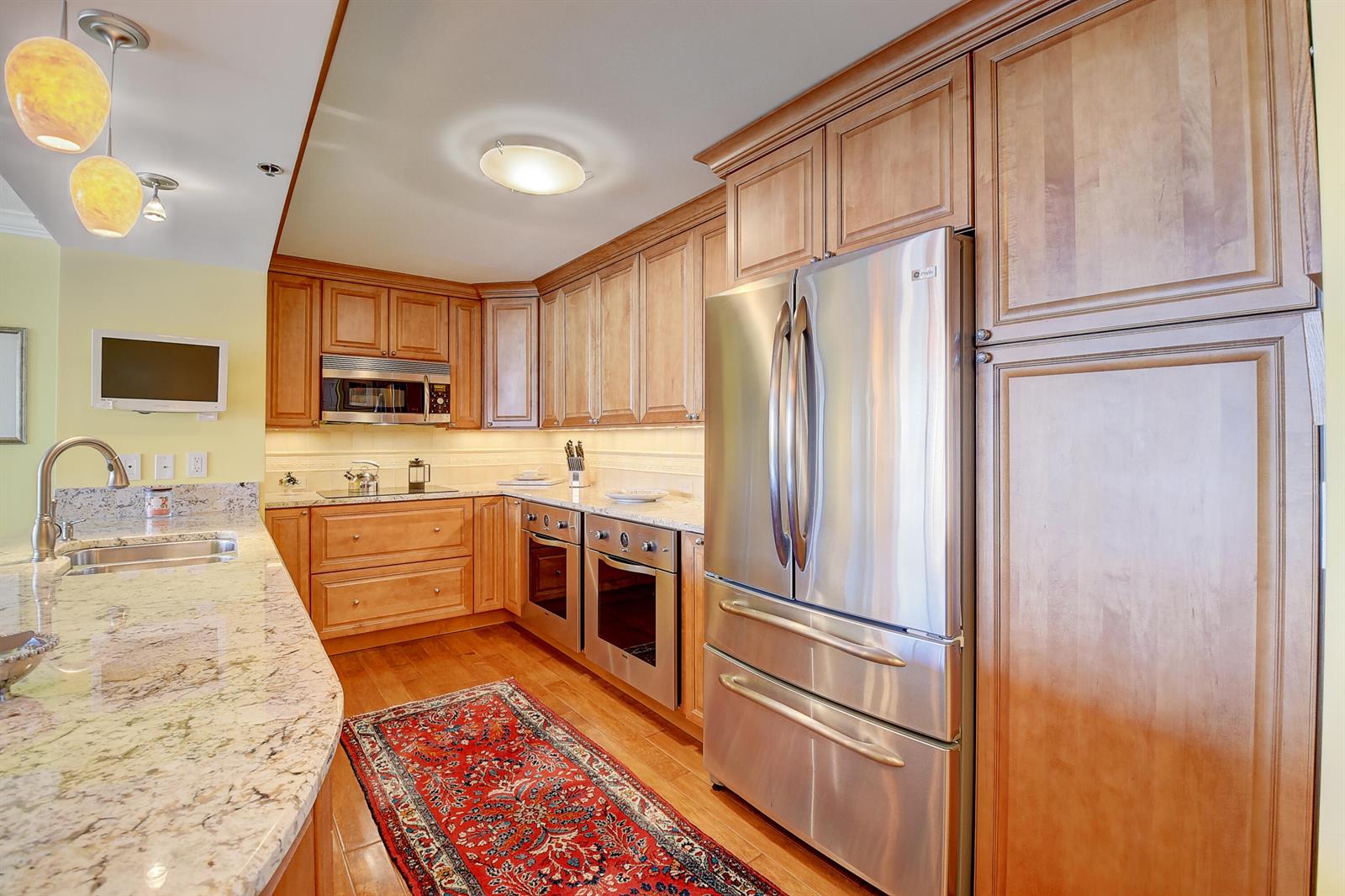 A kitchen with wood cabinets, stainless steel appliances, granite countertops, and a red area rug — 4750 S Ocean Boulevard # 702, Highland Beach FL 33487, HIGHLAND BEACH, FL