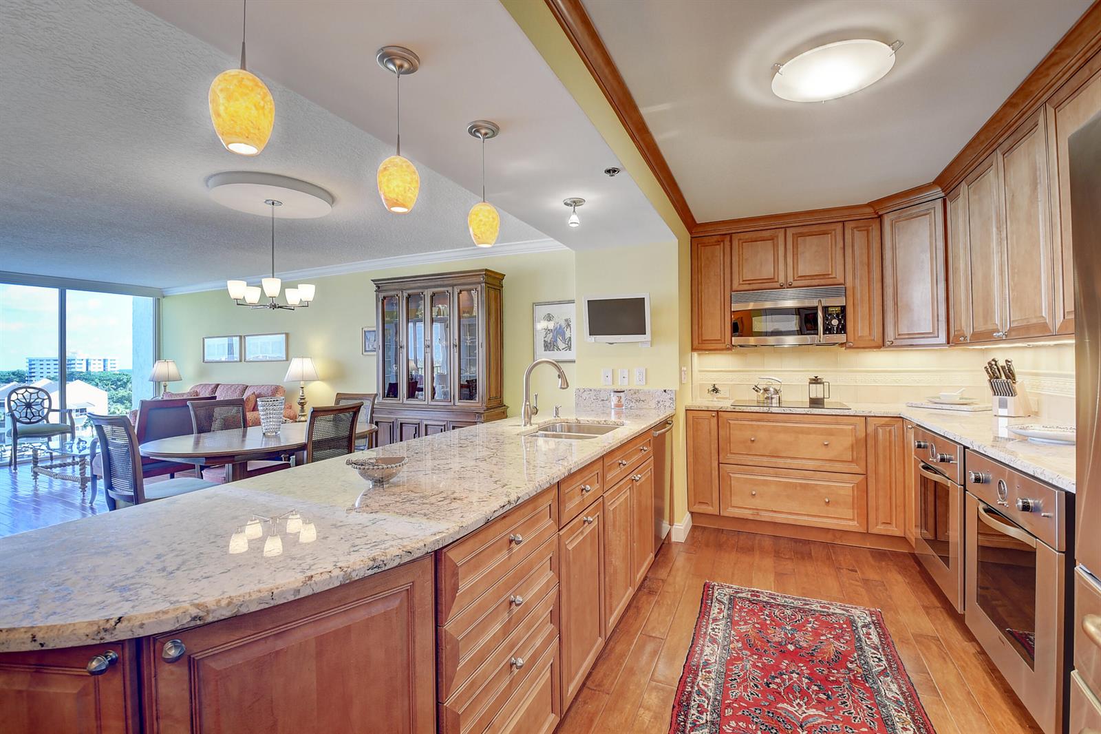 A kitchen with granite countertops, wood cabinets, and stainless steel appliances overlooks a dining area — 4750 S Ocean Boulevard # 702, Highland Beach FL 33487, HIGHLAND BEACH, FL