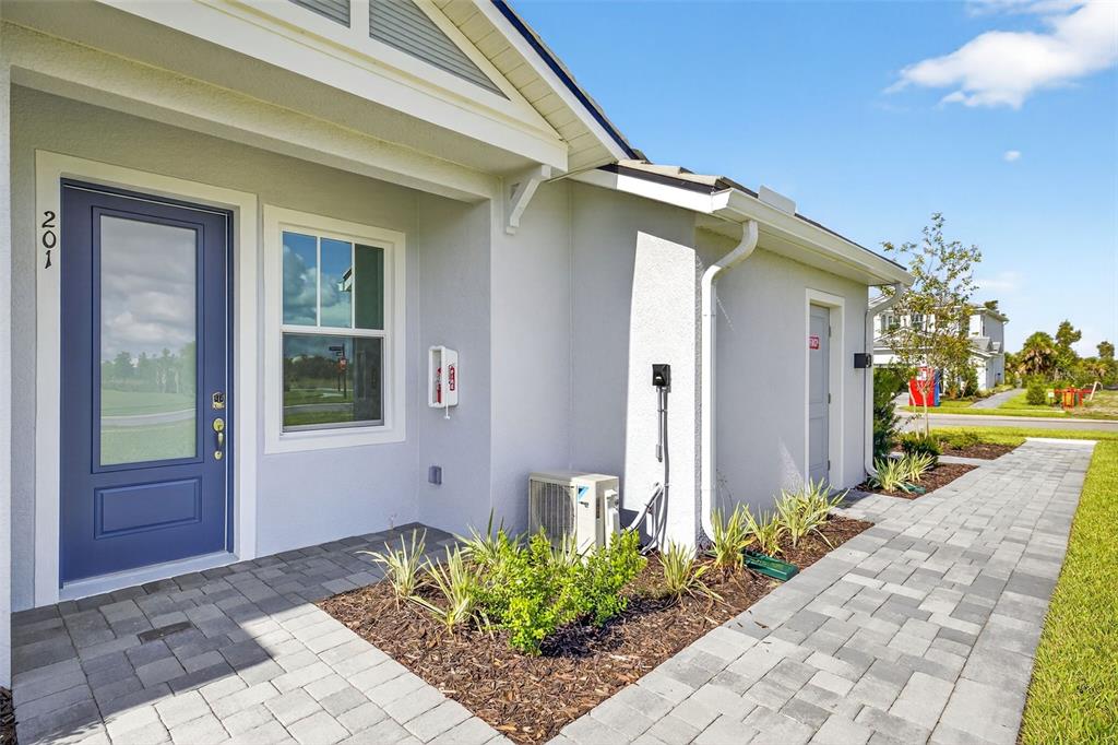 The exterior of a house features a blue front door, a paver walkway, and landscaping — 17420 MOONFLOWER DRIVE UNIT 201, VENICE, FL