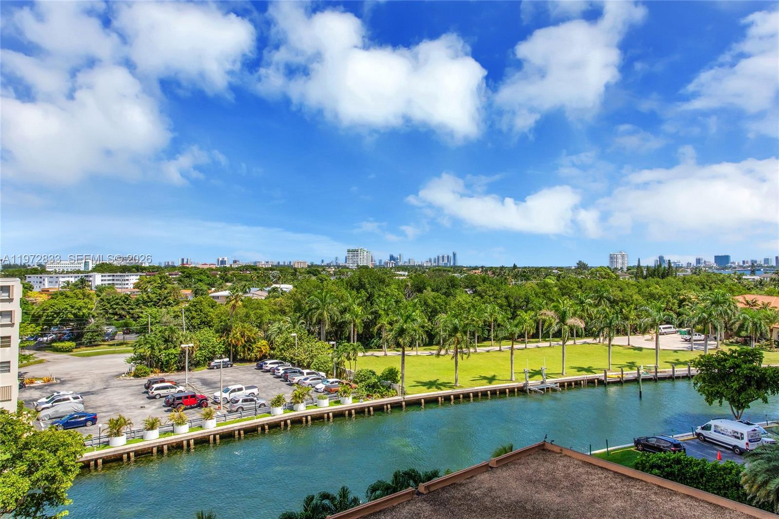 An elevated view of a canal, a parking lot, palm trees, and a distant city skyline — 1800 NE 114th St # 711, Miami FL 33181, MIAMI, FL