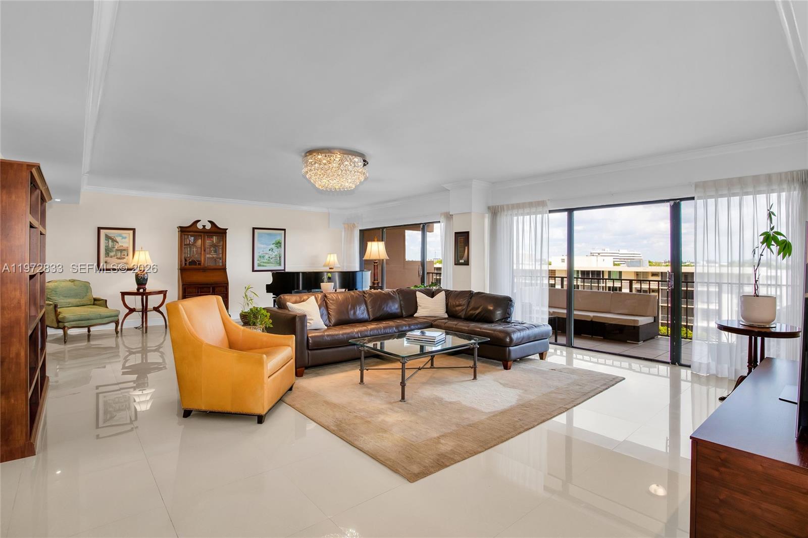 A spacious living room features a leather sectional, an orange armchair, and a balcony view — 1800 NE 114th St # 711, Miami FL 33181, MIAMI, FL
