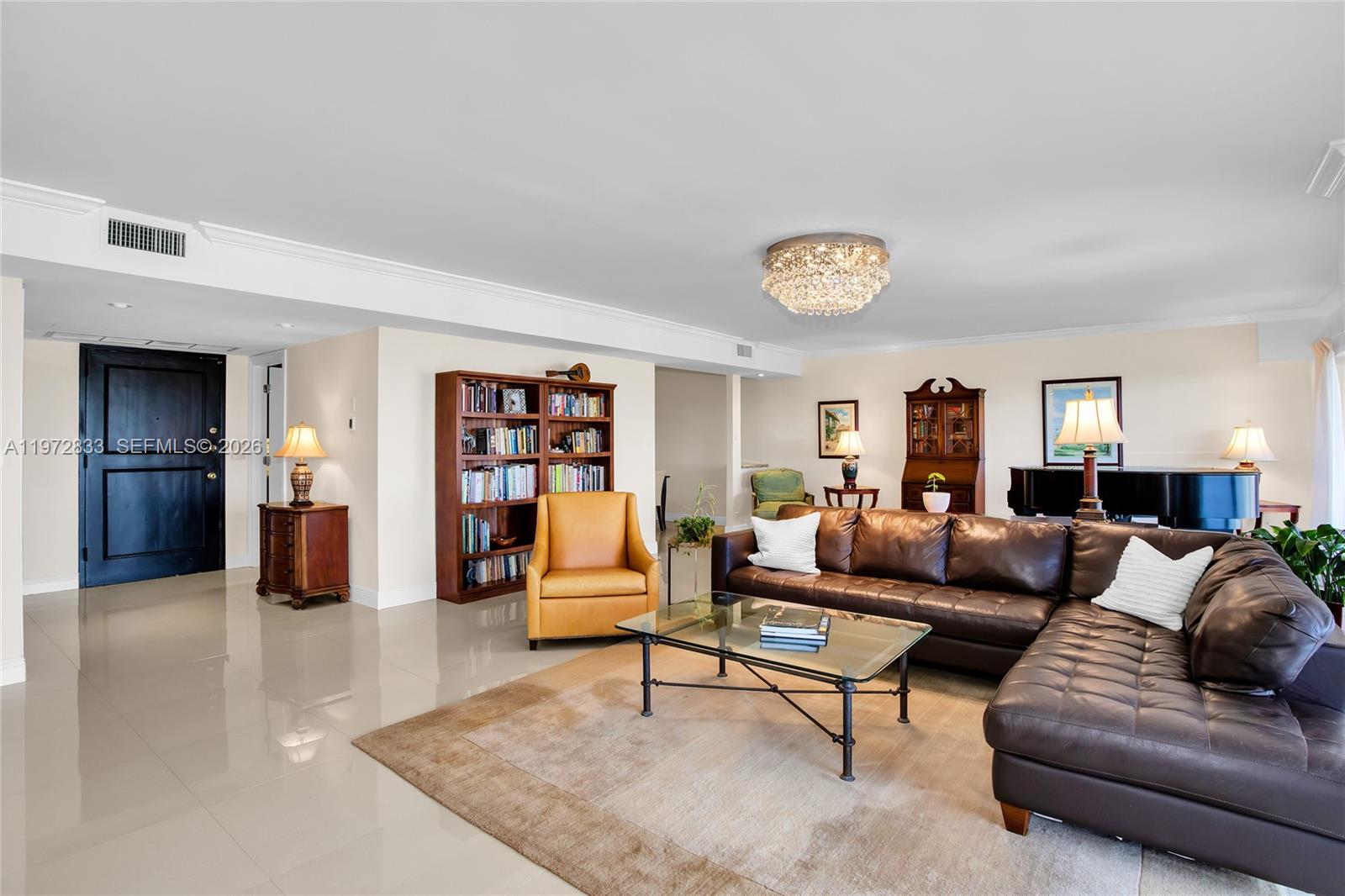 A spacious living room features a brown leather sectional, glass coffee table, and bookshelf — 1800 NE 114th St # 711, Miami FL 33181, MIAMI, FL