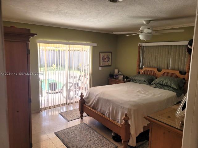 A bedroom features a wooden bed frame, tile flooring, and sliding glass doors to a patio — 270 SE 1st Ter, Pompano Beach FL 33060, POMPANO BEACH, FL