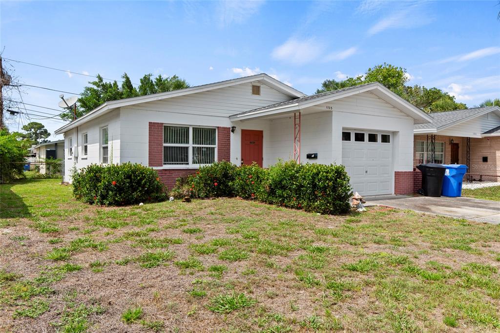A single-story white house with a red door, brick accents, and an attached garage — 1735 MISSISSIPPI AVENUE NE, ST PETERSBURG, FL