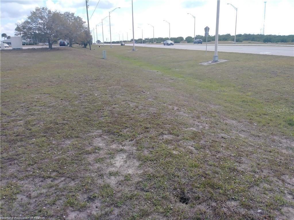 A grassy, sloping lot sits adjacent to a paved road with streetlights and distant trees — 1503 US 27 S, LAKE PLACID, FL