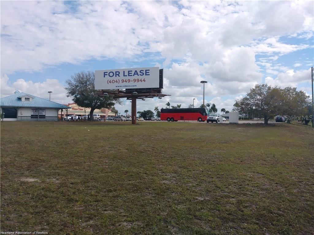 A large, vacant grassy lot features a billboard for lease and a nearby shopping center — 1503 US 27 S, LAKE PLACID, FL