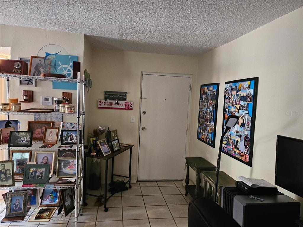 A room with tile flooring, a white door, a metal shelving unit, and wall-mounted photo collages — 2613 PINE LAKE TER UNIT B, SARASOTA, FL