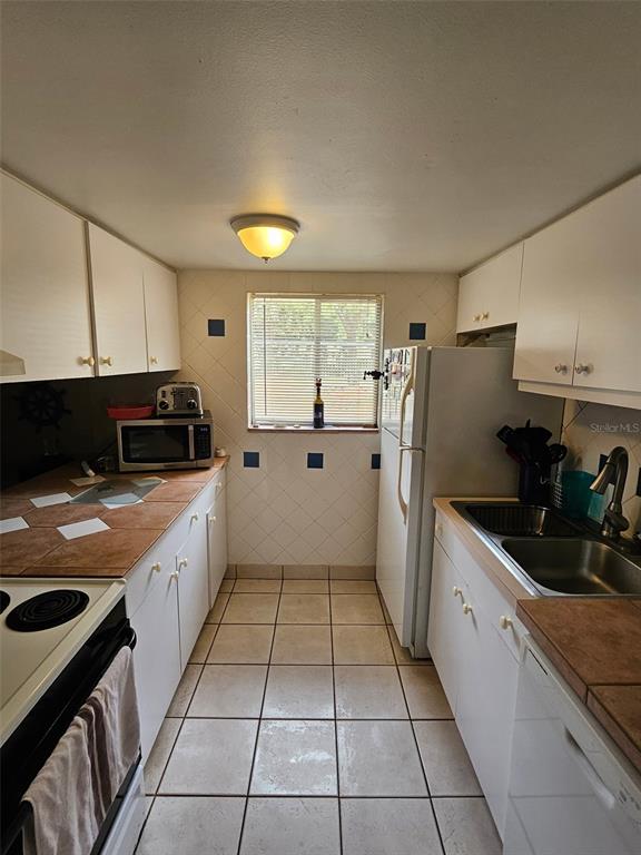 A galley-style kitchen features white cabinets, tiled countertops, a window, and a white refrigerator — 2613 PINE LAKE TER UNIT B, SARASOTA, FL