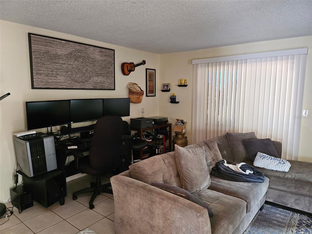 A living room features a desk with three monitors, a sofa, and vertical window blinds — 2613 PINE LAKE TER UNIT B, SARASOTA, FL