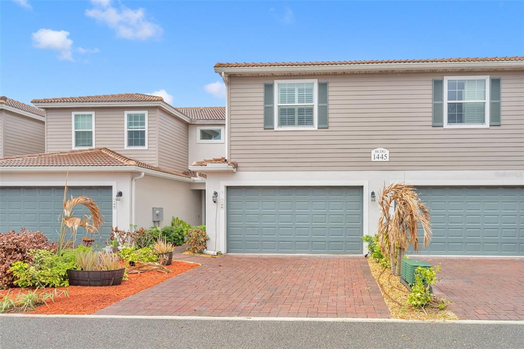 A two-story townhouse exterior features beige siding, a brick driveway, and gray garage doors — 1445 ISABELLA DRIVE UNIT 105, MELBOURNE, FL