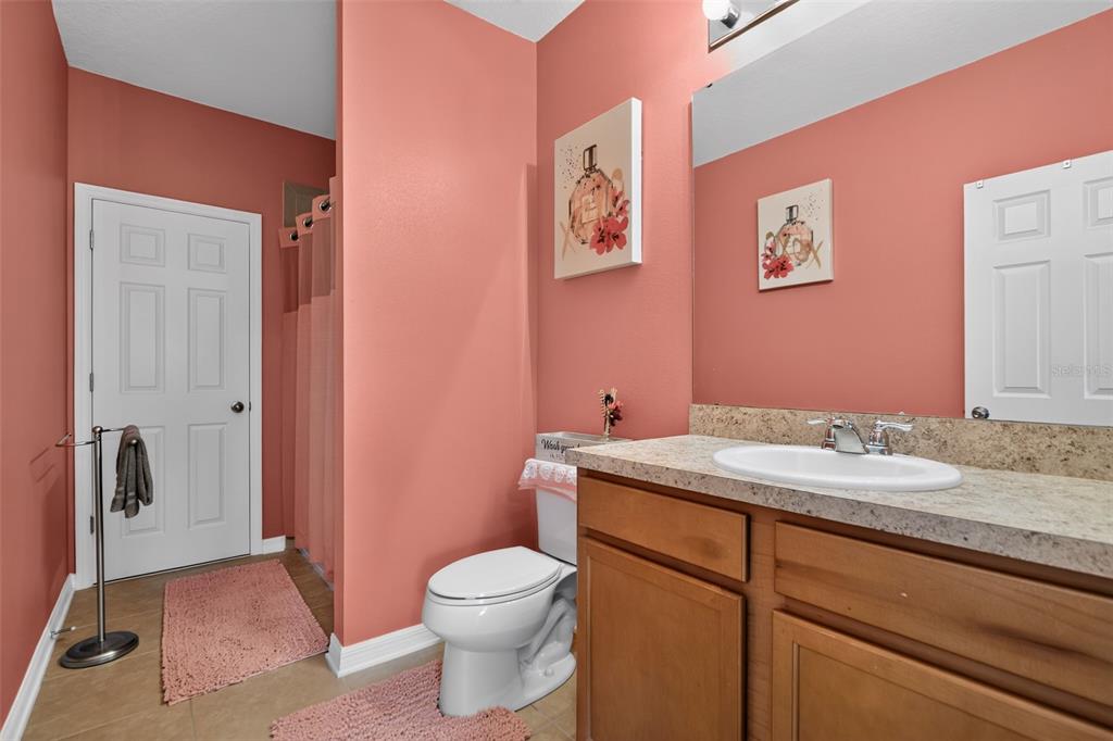 A bathroom features coral walls, a wood vanity with a stone countertop, and a toilet — 5863 CYPRESS HILL ROAD, WINTER GARDEN, FL
