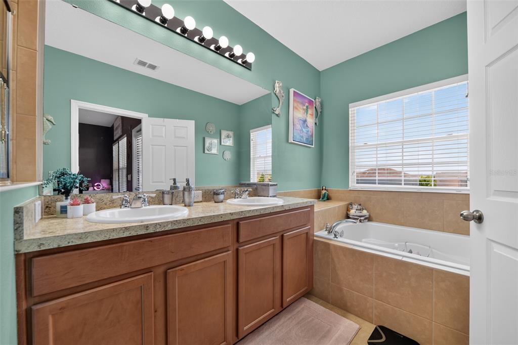 A bathroom features a double vanity with a granite countertop, a soaking tub, and teal walls — 5863 CYPRESS HILL ROAD, WINTER GARDEN, FL