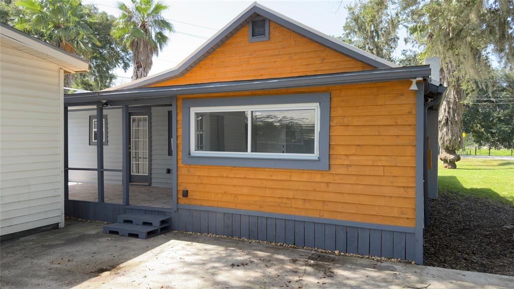 A small house with orange horizontal siding, a gray-trimmed window, and a screened-in porch — 14740 JOHNS ROAD, DADE CITY, FL