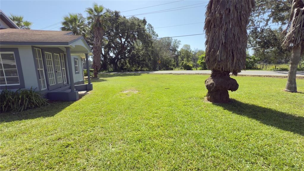 A view of a grassy yard next to a house with a covered porch — 14740 JOHNS ROAD, DADE CITY, FL