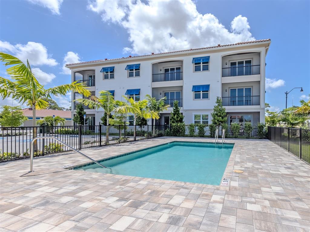A rectangular swimming pool sits on a paved patio beside a multi-story apartment building — 787 S. TAMIAMI TRAIL UNIT 101, VENICE, FL