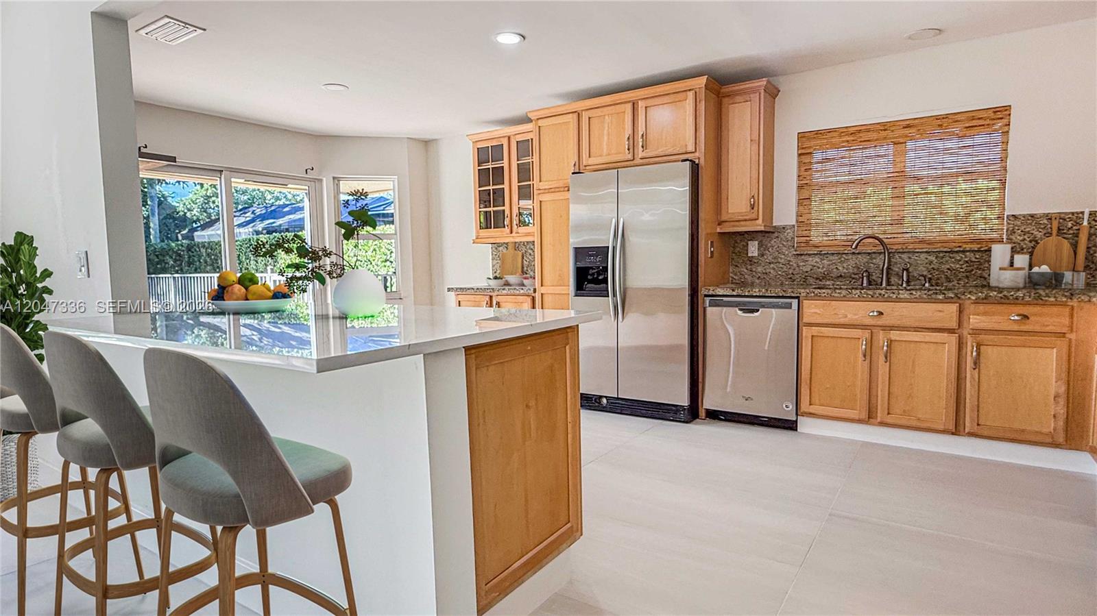 A kitchen features light wood cabinets, stainless steel appliances, a white island, and gray stools — 10134 Boca Woods Ln # 1034, Boca Raton FL 33428, BOCA RATON, FL