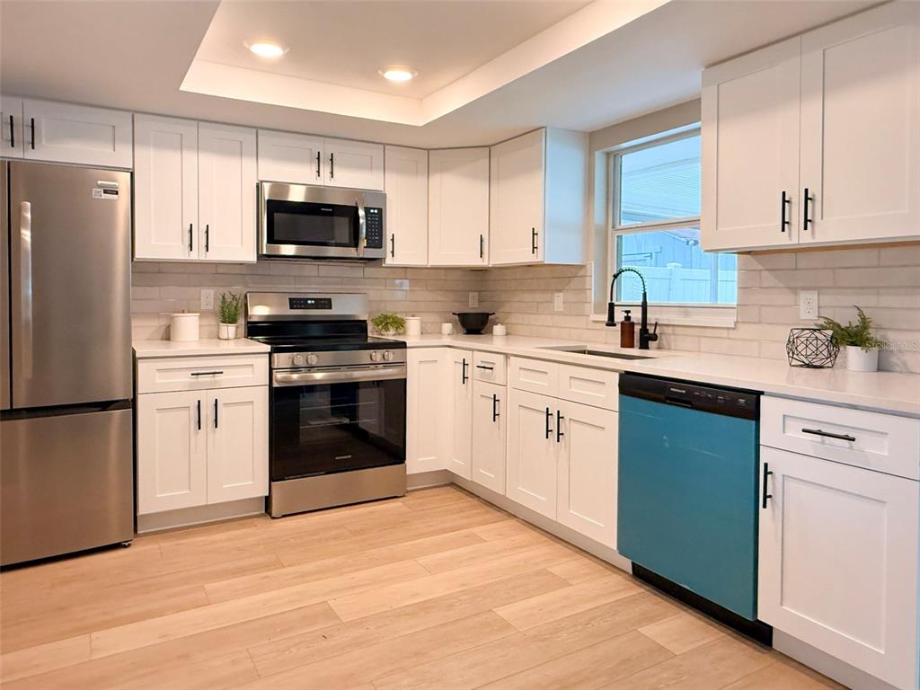 A kitchen features white cabinets, stainless steel appliances, a blue dishwasher, and light wood flooring — 12635 NICOLE LANE, TAMPA, FL
