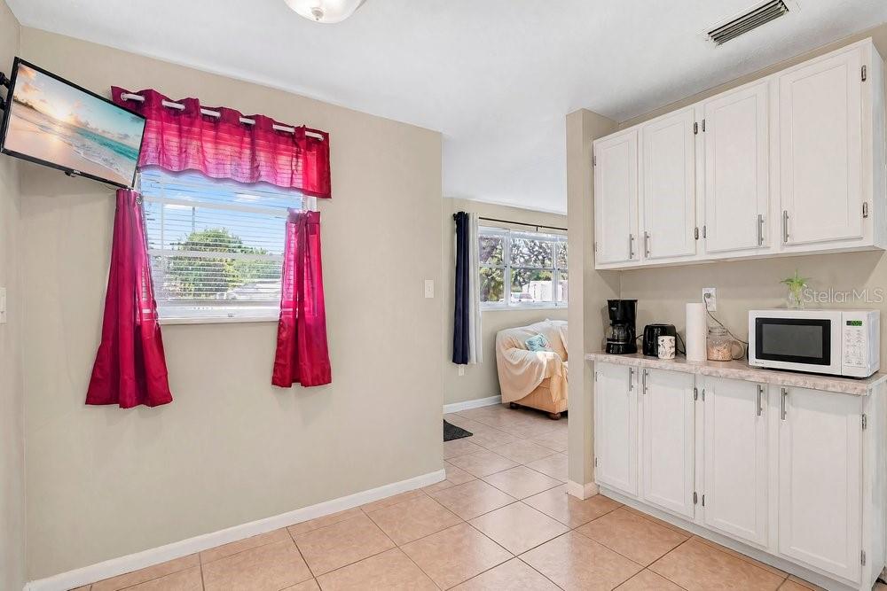 A kitchen with white cabinets and tile flooring opens into a living area with windows — 218 DENNIS AVENUE, WINTER HAVEN, FL