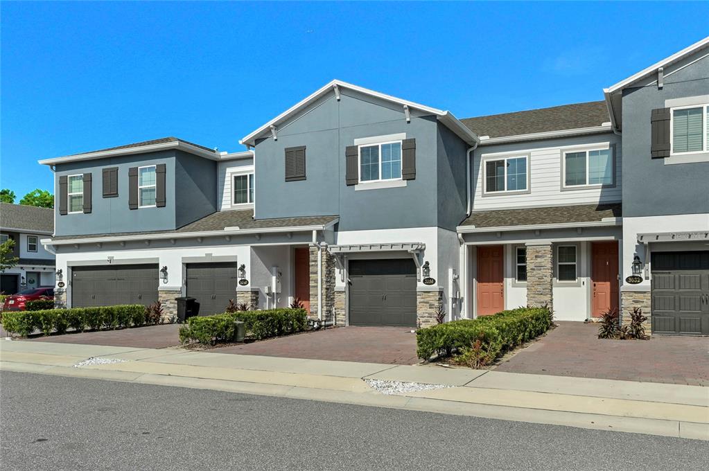 A row of multi-story townhomes features gray siding, stone accents, and attached garages — 3036 PILOT HOUSE PLACE, OVIEDO, FL
