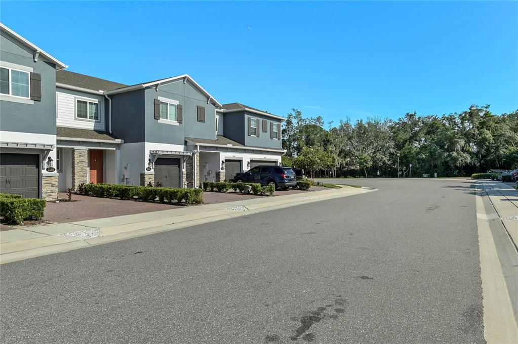 A street view of multi-story townhomes with attached garages and paved driveways under a blue sky — 3036 PILOT HOUSE PLACE, OVIEDO, FL