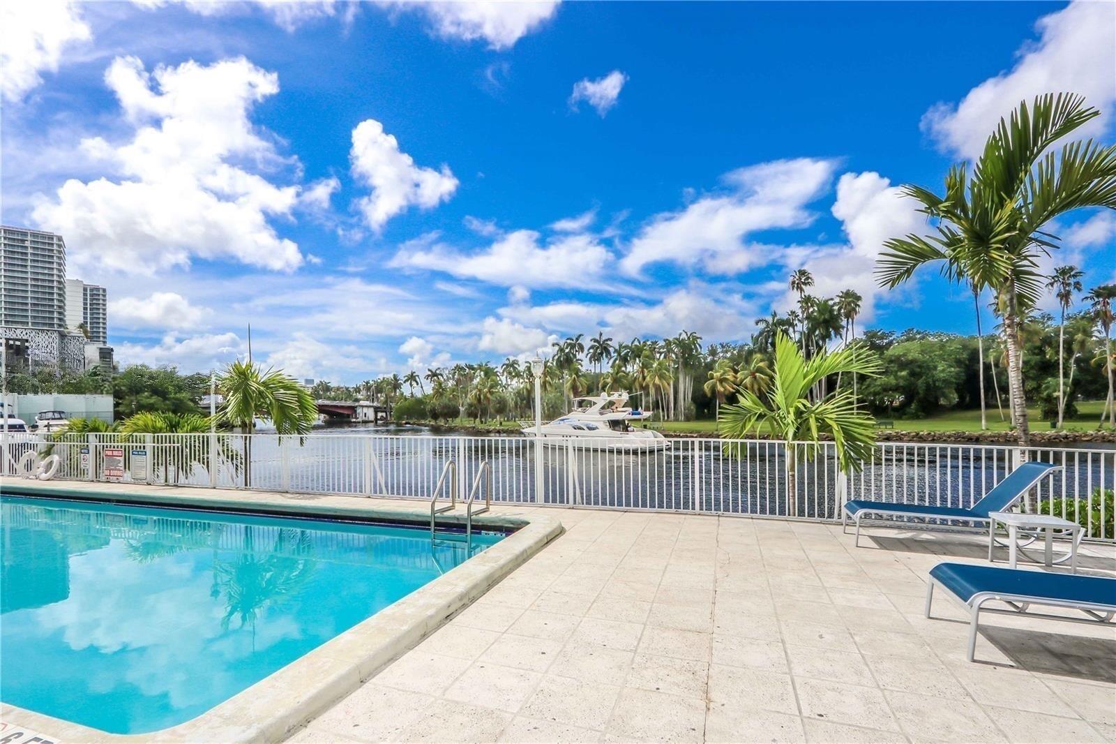 A swimming pool with lounge chairs overlooks a canal with a yacht and palm trees — 1740 NW N River Drive # 319, Miami FL 33125, MIAMI, FL