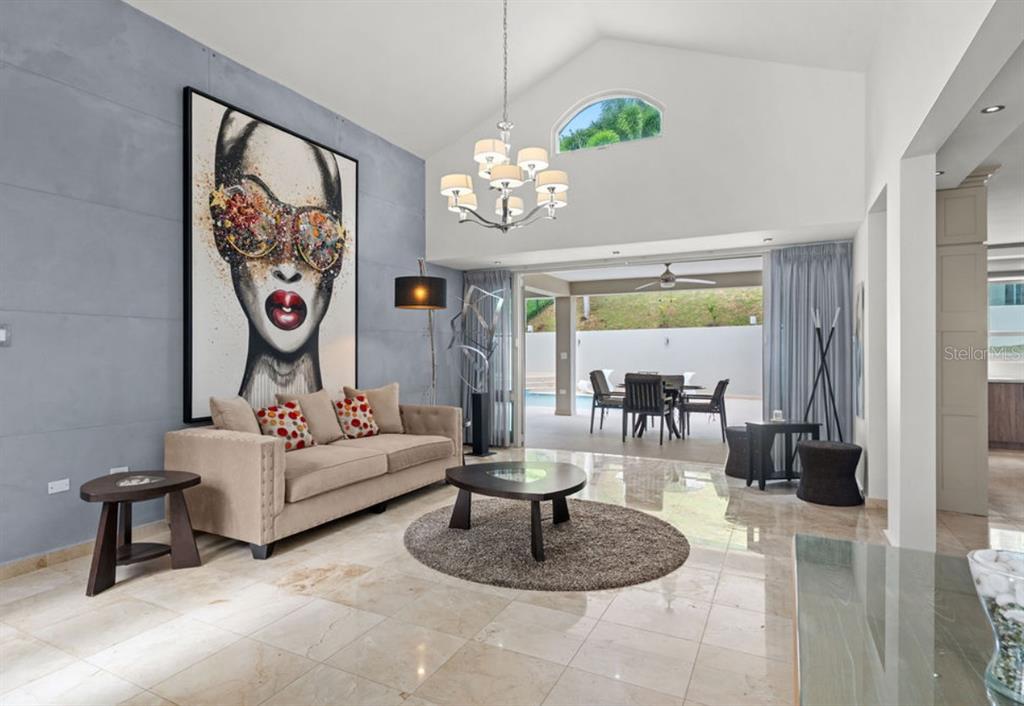A living room features a large portrait painting, a beige sofa, and glass doors to a patio — 1 ZORZAL, SAN JUAN, PR