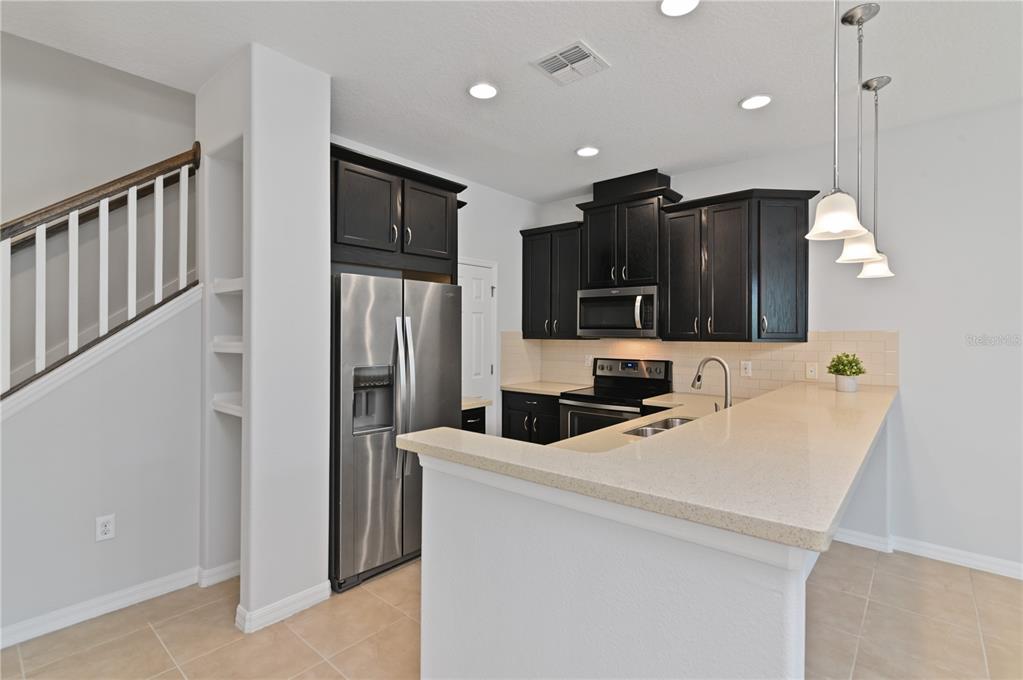 A kitchen features dark wood cabinets, stainless steel appliances, and a beige breakfast bar — 2913 WINDMILL DR, KISSIMMEE, FL