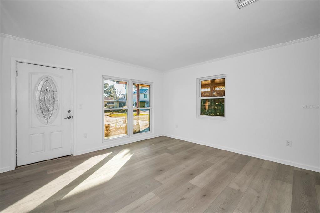 An empty room with white walls, light wood-look flooring, a front door, and two windows — 406 ORCHID LANE, PALM HARBOR, FL