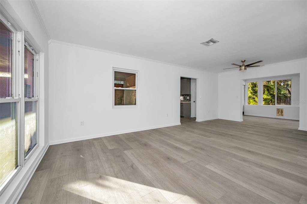 An empty living room with white walls, light wood-look flooring, and a ceiling fan — 406 ORCHID LANE, PALM HARBOR, FL
