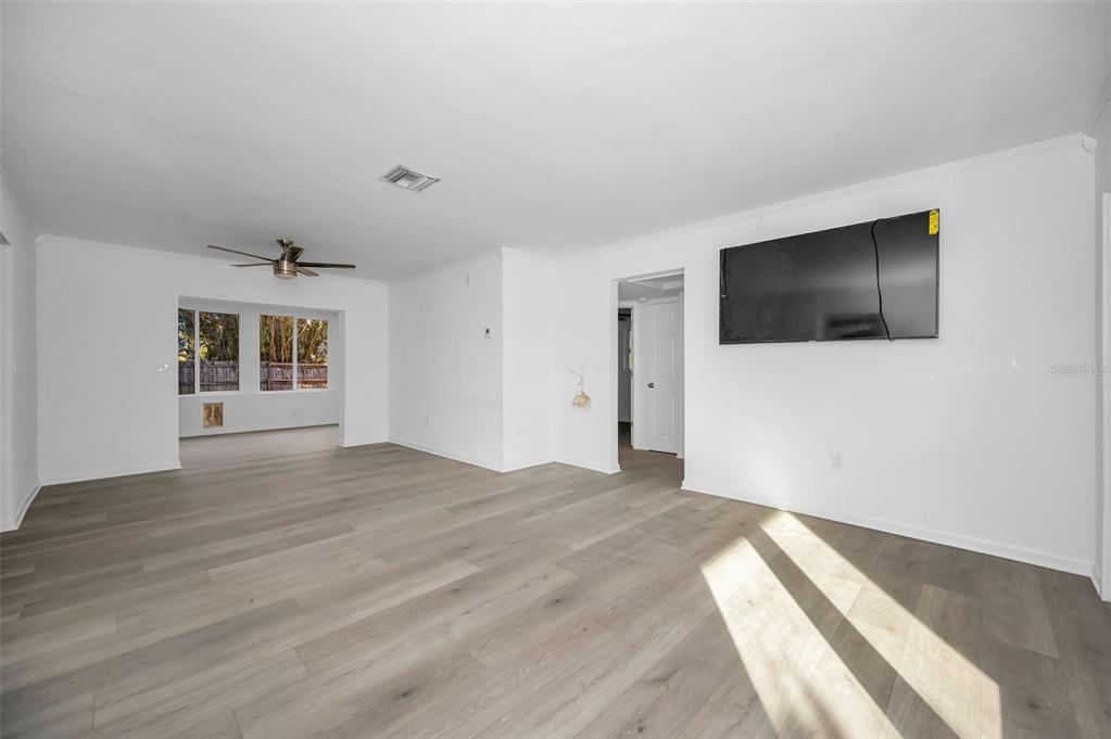 A living room with white walls, light wood-look flooring, a ceiling fan, and wall-mounted television — 406 ORCHID LANE, PALM HARBOR, FL