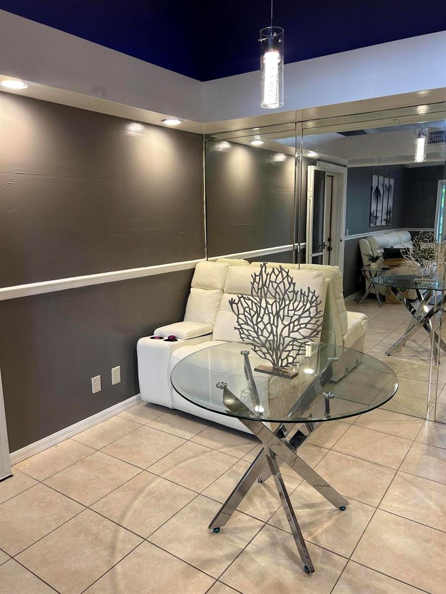 A glass-topped table and white recliner sit in a room with mirrored walls and tile — 1007 Green Pine Boulevard, West Palm Beach FL 33409, WEST PALM BEACH, FL