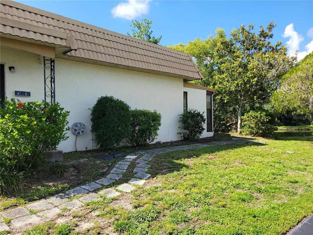 A side view of a house with a tan mansard roof and a stone walkway — 9110 VIA RECREO, NEW PORT RICHEY, FL