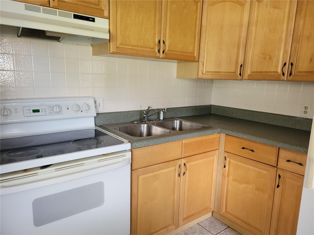 A kitchen features light wood cabinets, white appliances, a tiled backsplash, and gray countertops — 9110 VIA RECREO, NEW PORT RICHEY, FL