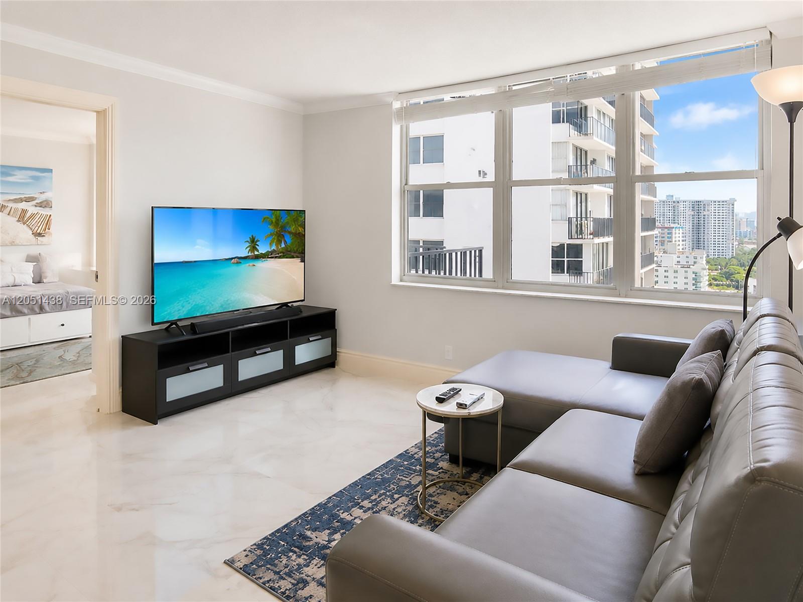 A living room features a grey sectional sofa, a television on a stand, and windows — 2201 S Ocean Dr # 2005, Hollywood FL 33019, HOLLYWOOD, FL