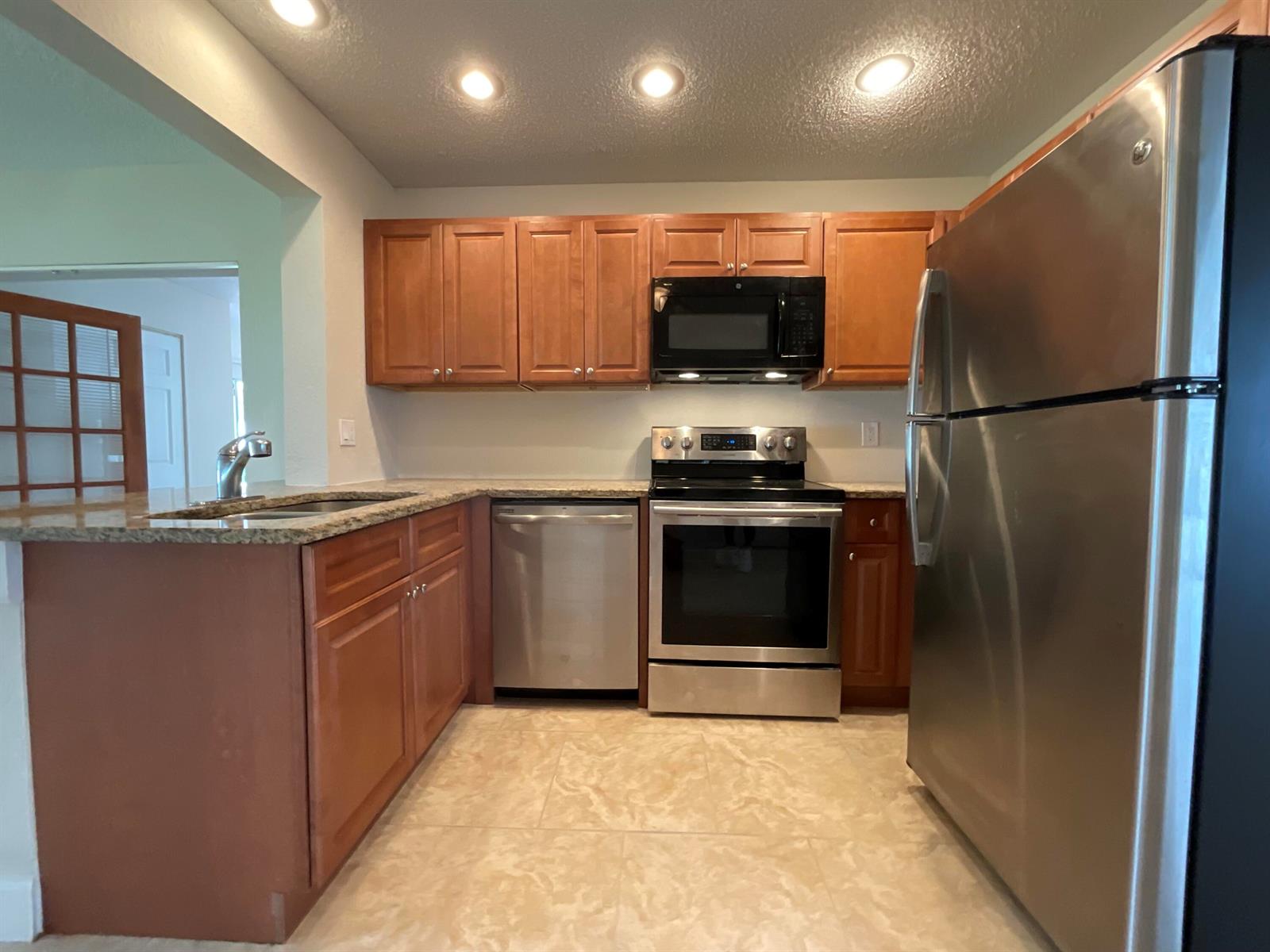 A kitchen features wood cabinets, stainless steel appliances, granite countertops, and tile flooring — 2016 SW 16th Avenue, Boynton Beach FL 33426, BOYNTON BEACH, FL