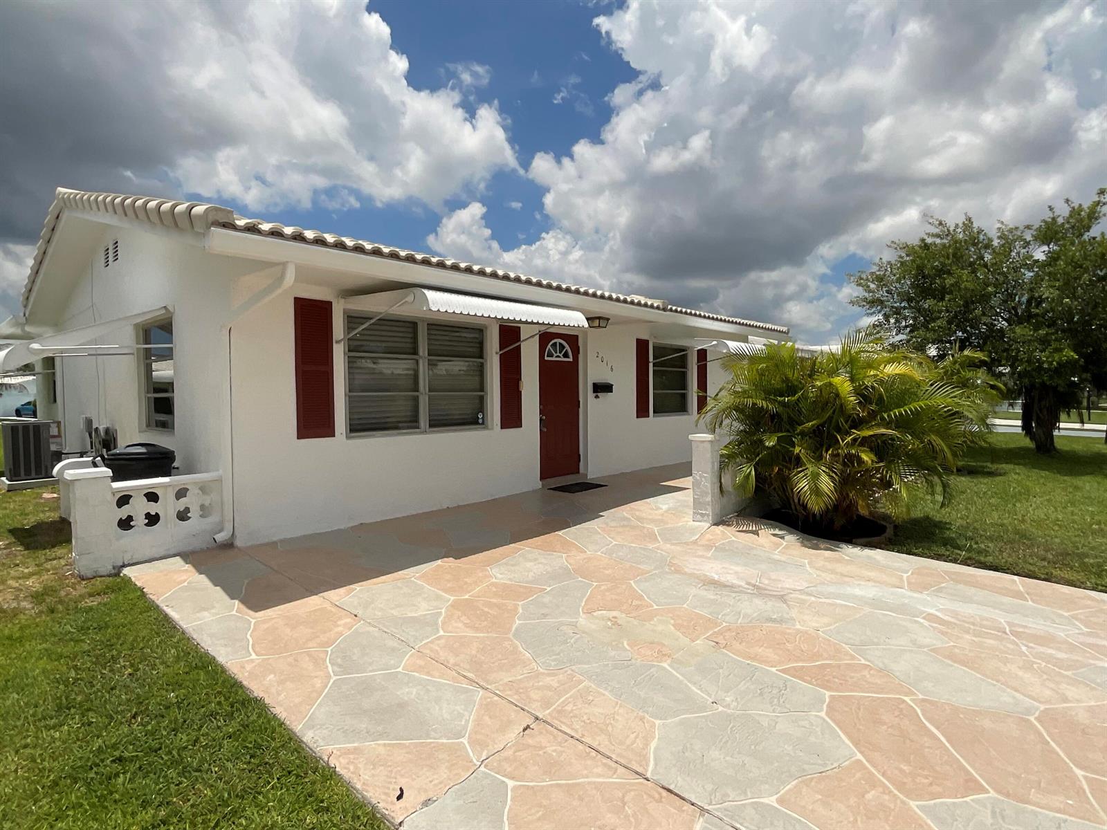 A white house with red shutters and a stone-patterned driveway under a cloudy sky — 2016 SW 16th Avenue, Boynton Beach FL 33426, BOYNTON BEACH, FL