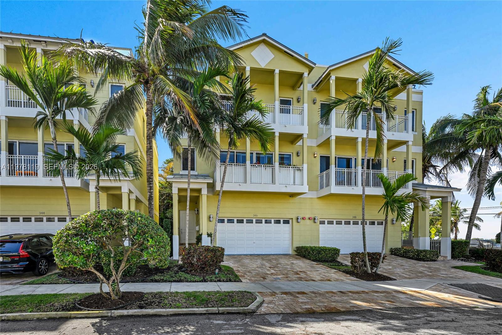 A three-story yellow townhouse with balconies, a two-car garage, and palm trees in front — 346 Elm St # 10, Hollywood FL 33019, HOLLYWOOD, FL