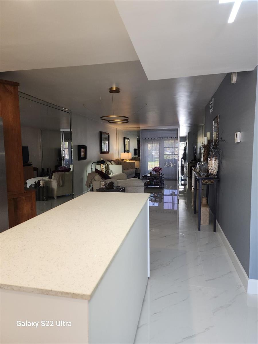 A kitchen island with a light countertop overlooks a living area with mirrored walls — 700 SE 6th Avenue # 111, Deerfield Beach FL 33441, DEERFIELD BEACH, FL