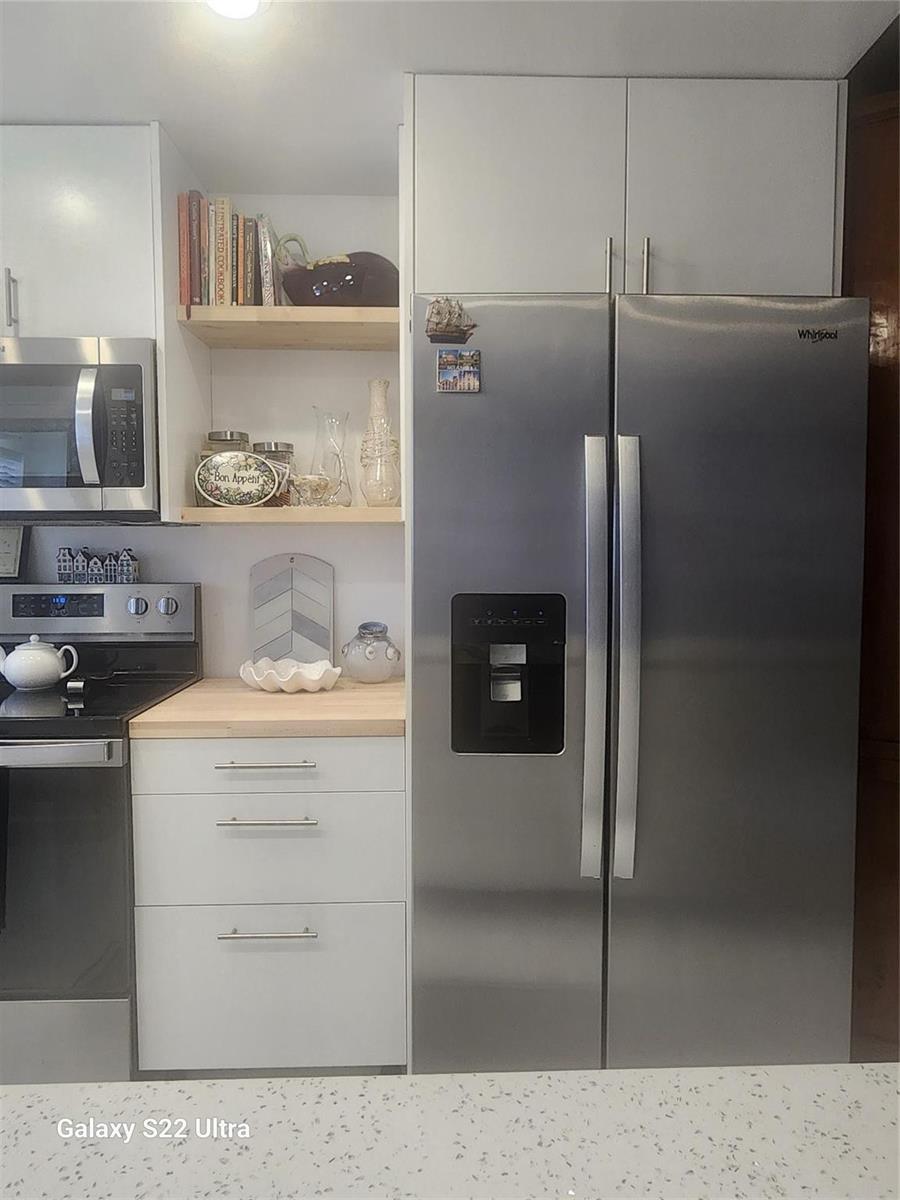 A kitchen features white cabinets, a stainless steel refrigerator, and open wood shelving — 700 SE 6th Avenue # 111, Deerfield Beach FL 33441, DEERFIELD BEACH, FL